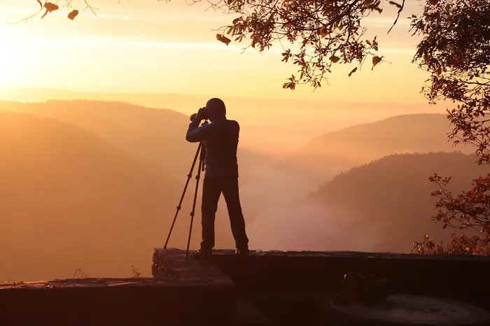 Person mit Kamera beobachtet eine Landschaft bei Sonnenaufgang